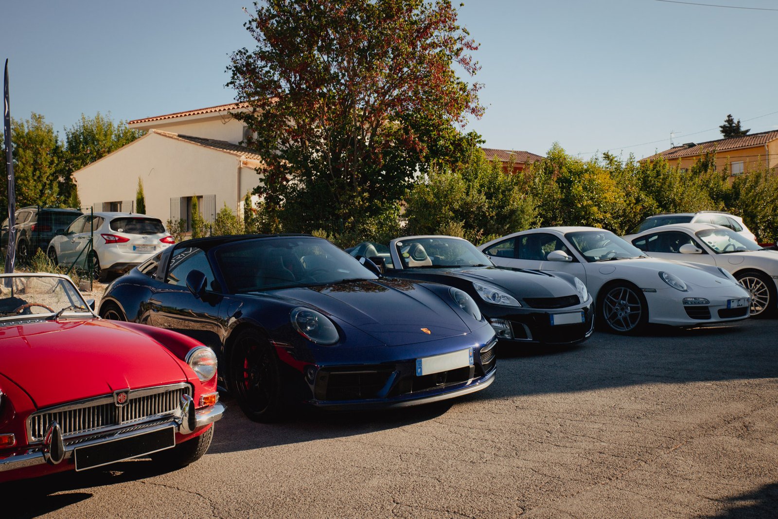 MG B rouge, Porsche 911 bleue et cabriolet noir réunis lors du rassemblement automobile.