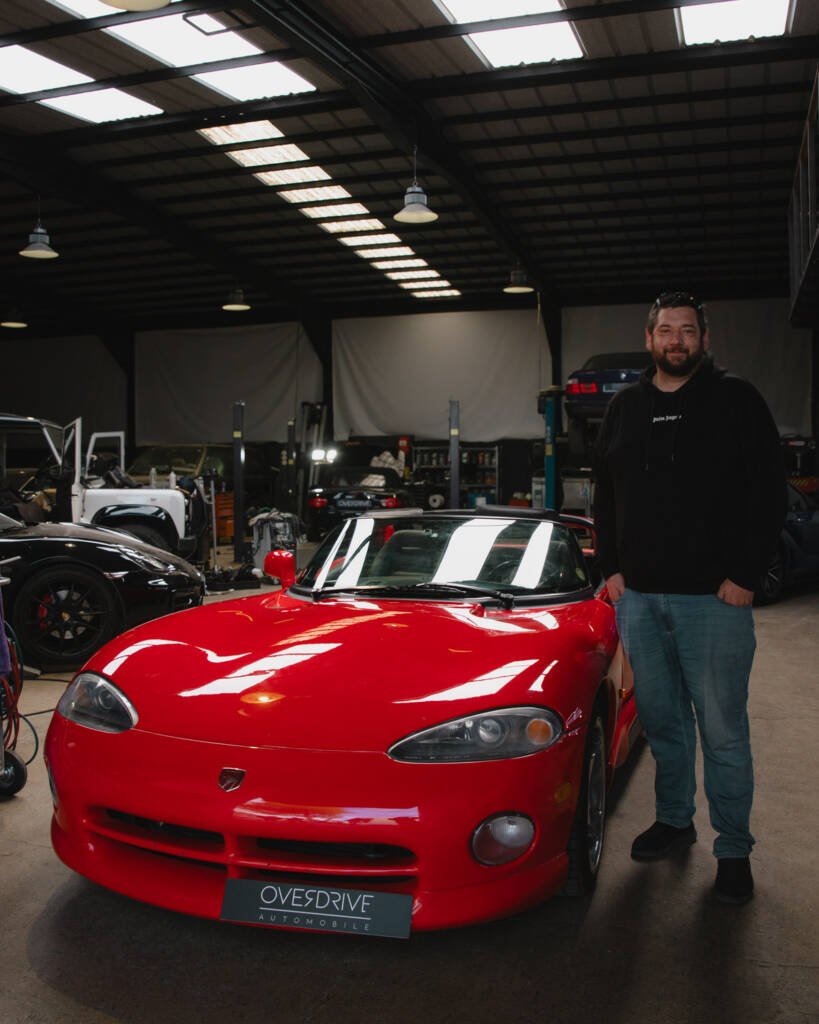 Nicolas debout aux côtés de sa Chrysler Viper RT/10 de 1993 dans l'atelier Overdrive Automobile.